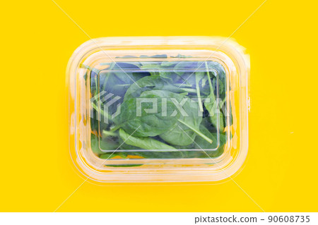 Spinach leaves in plastic box on yellow background. Spinach leaves in plastic box on yellow background. 90608735