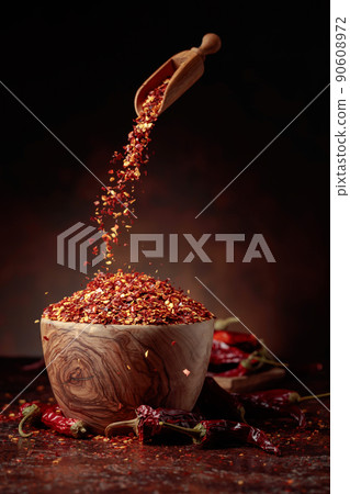 Chilli flakes are poured into a wooden dish. 90608972