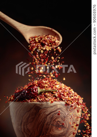 Chilli flakes are poured into a wooden dish. Chilli flakes are poured into a wooden dish. 90608976