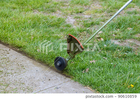 Worker in cutting grass the near pavement with using string lawn trimmer Worker in cutting grass the near pavement with using string lawn trimmer 90610859