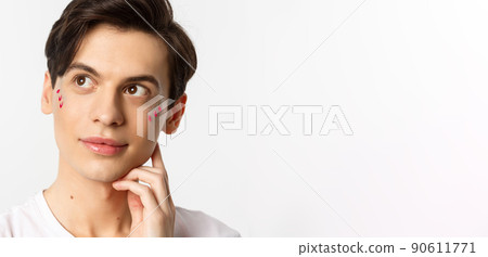 People, lgbtq and beauty concept. Close-up of happy queer man with applied lip gloss and glitter, smiling and looking at upper left corner, standing over white background People, lgbtq and beauty concept. Close-up of happy queer man with applied lip gloss and glitter, smiling and looking at upper left corner, standing over white background 90611771