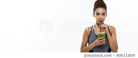 Healthy and Fitness concept - Beautiful American African lady in fitness clothing drinking healthy vegetable drink. Isolated on white background. 90611809