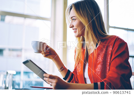 Cheerful hipster girl with perfect smile on face using digital tablet in coffee shop Cheerful hipster girl with perfect smile on face using digital tablet in coffee shop 90613741