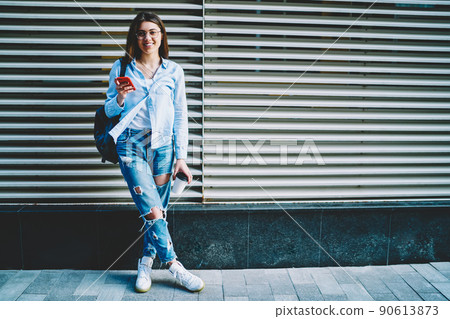 Cheerful young hipster girl holding mobile phone and coffee to go during trip vacations Cheerful young hipster girl holding mobile phone and coffee to go during trip vacations 90613873