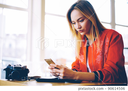 Millennial female blogger uploading pictures and videos to web page using mobile internet 90614506