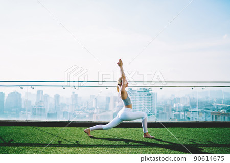 Woman doing crescent lunge on rooftop in sunny morning 90614675