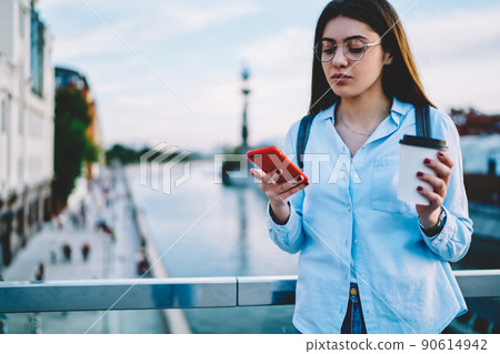 Young woman blogger in spectacles checking mail and sending messages via smartphone 90614942
