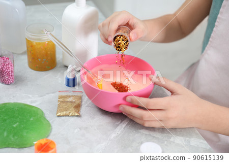 Little girl adding colored sparkles into homemade slime toy at table, closeup of hands Little girl adding colored sparkles into homemade slime toy at table, closeup of hands 90615139
