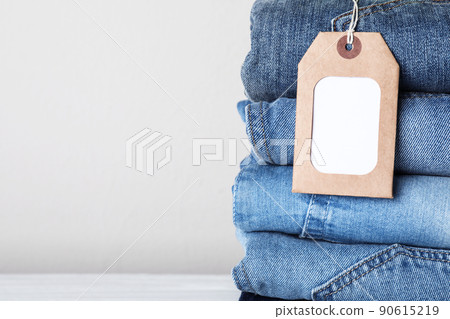Stack of different jeans with tag on light background, closeup. Space for text 90615219