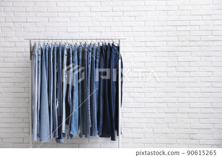 Rack with stylish jeans near brick wall. Space for text 90615265