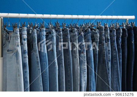 Rack with stylish jeans on blue background, closeup Rack with stylish jeans on blue background, closeup 90615276