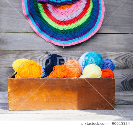 Knitted colorful striped mats and balls of bright woolen yarn in a wooden box on old wood wall background Knitted colorful striped mats and balls of bright woolen yarn in a wooden box on old wood wall background 90615524