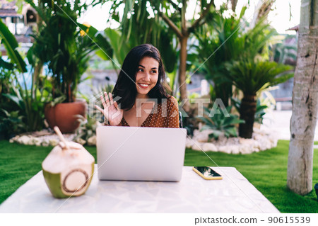 Pretty young Asian woman using laptop and waving hello in outdoor cafe 90615539
