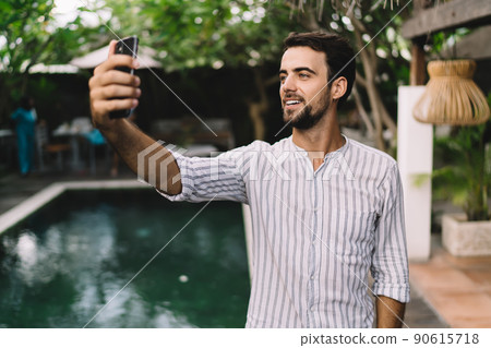 Cheerful young man taking self portrait on smartphone during summer holidays Cheerful young man taking self portrait on smartphone during summer holidays 90615718