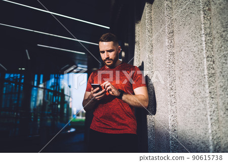 Serious man surfing cellphone against wall Serious man surfing cellphone against wall 90615738