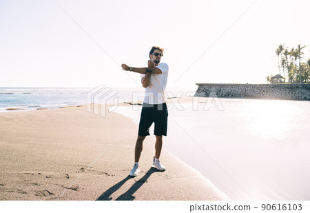 Young man doing stretching exercises on beach 90616103