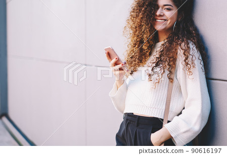 Portrait of happy curly hipster girl with mobile phone in hand posing at street 90616197