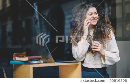 Cheerful hipster girl with laptop computer enjoying friendly mobile talking Cheerful hipster girl with laptop computer enjoying friendly mobile talking 90616206
