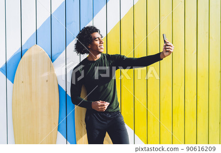 Handsome dark skinned african american male surfboarder posing for selfie on smartphone camera 90616209