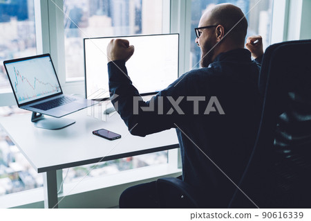 Excited broker celebrating victory while watching multimedia gadgets in office Excited broker celebrating victory while watching multimedia gadgets in office 90616339