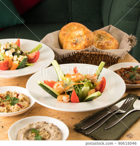Dining table full of delicious salad on a white plate next to basket of bread Dining table full of delicious salad on a white plate next to basket of bread 90618046