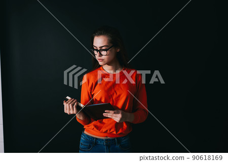 Serious woman reading notebook in dark room Serious woman reading notebook in dark room 90618169