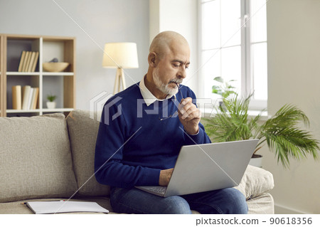 Senior man sitting on couch at home, working on his laptop computer and thinking Senior man sitting on couch at home, working on his laptop computer and thinking 90618356