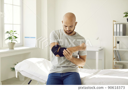 Man puts on bandage on injured elbow which serves to restore and relieve joint pain. Man puts on bandage on injured elbow which serves to restore and relieve joint pain. 90618373