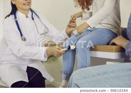 Neurology specialist examining little child and using hammer to test knee reflex 90618384