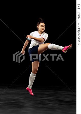 Young caucasian sportive woman, female soccer, football player in motion isolated on dark background. Sport, action, competitions, games and fitness concept Young caucasian sportive woman, female soccer, football player in motion isolated on dark background. Sport, action, competitions, games and fitness concept 90619131