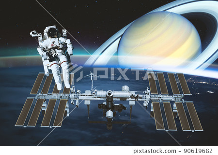 Astronaut performs spacewalk over the international space station while fantasy in the background sees the planet saturn. Elements of this image furnished by NASA. 90619682