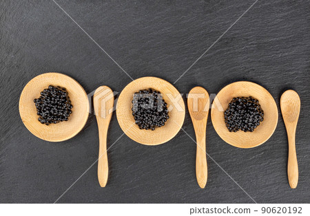 Wooden mini plates with black caviar on a stone board for serving and wooden mini spoons. Wooden mini plates with black caviar on a stone board for serving and wooden mini spoons. 90620192