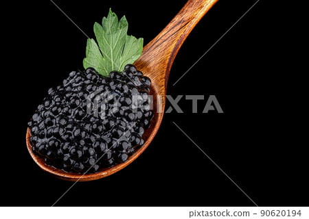 Close-up of a wooden spoon full of black caviar with a parsley leaf on a black background. Close-up of a wooden spoon full of black caviar with a parsley leaf on a black background. 90620194