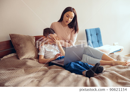 Mother lying on bed with little son and watching scary movie on laptop. Mother lying on bed with little son and watching scary movie on laptop. 90621154