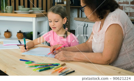7-year Old Little Girl Doing School Homework with Grandma while Sitting at Table in the Kitchen. Education, Teaching, Learning and People Concept 7-year Old Little Girl Doing School Homework with Grandma while Sitting at Table in the Kitchen. Education, Teaching, Learning and People Concept 90621224