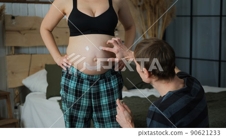 Male Drawing Funny Smiley Face on Belly of his Pregnant Wife at Home. Family Preparing for Newborn Male Drawing Funny Smiley Face on Belly of his Pregnant Wife at Home. Family Preparing for Newborn 90621233