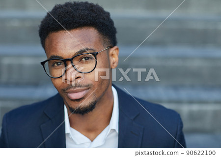 Portrait of content handsome young smart African-American man in eyeglasses sitting on staircase outdoors 90622100
