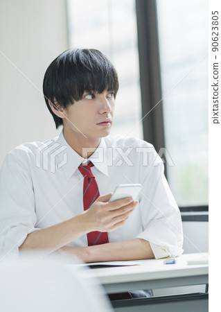 Male high school student looking at a smartphone in the classroom 90623805