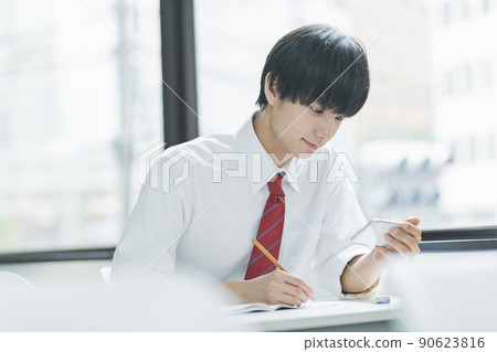 Male high school student looking at a smartphone in the classroom 90623816