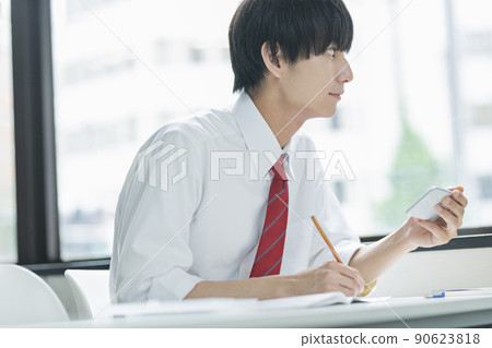 Male high school student looking at a smartphone in the classroom 90623818