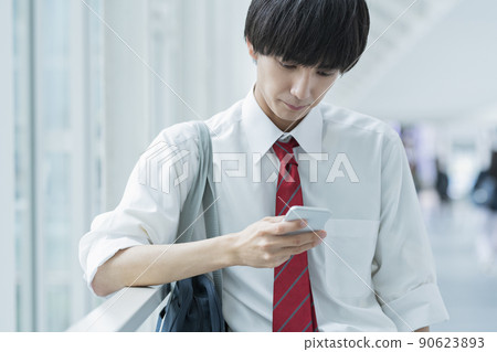High school boy looking at a mobile phone while commuting to school 90623893