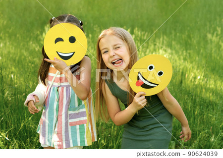 Two cute girl friends are making faces and grimacing, holding in their hands the crazy and winking emoticons 90624039