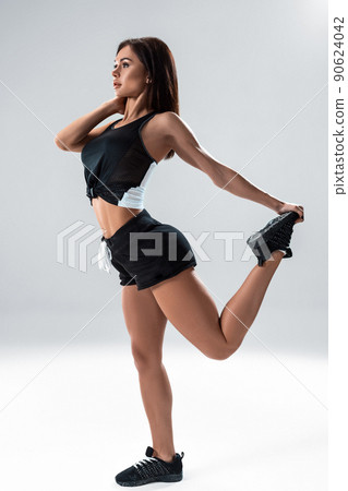 Beautiful brunette woman stretching her legs, warm up on grey background Beautiful brunette woman stretching her legs, warm up on grey background 90624042