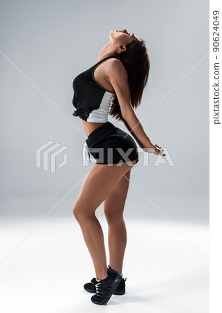Slim and sport young woman posing and doing sport exercises standing with her back to the camera and stretching arms in studio isolated over gray background 90624049