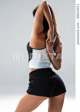 Slim and sport young woman posing and doing sport exercises standing with her back to the camera and stretching arms in studio isolated over gray background 90624051