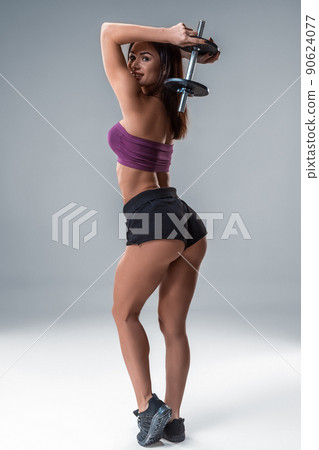 Studio portrait of a sporty young woman posing with dumbbell against a gray background Studio portrait of a sporty young woman posing with dumbbell against a gray background 90624077