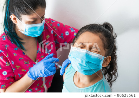 children's nurse injecting brown girl's arm. doctor injecting covid-19 vaccine. girl closes her eyes from severe pain and looks away, flu shot. medical concept, health and pandemic. 90625561