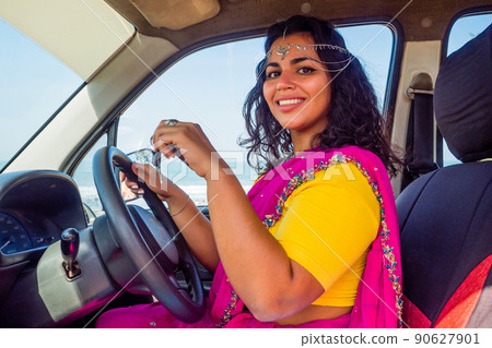 relaxed indian woman in a traditional pink sari and costume jewelry on summer travel vacation to the coast towards the sea 90627901