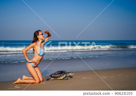travel girl posing in blue bikini swimsuit looking into the distance and pointing a finger next to a big male turtle lifestyle vacation paradise untouched deserted beach morning.tourism guide concept travel girl posing in blue bikini swimsuit looking into the distance and pointing a finger next to a big male turtle lifestyle vacation paradise untouched deserted beach morning.tourism guide concept 90628105