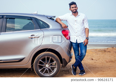 Indian businessman standing near car outdoors on sea beach summer good day.a man in a white shirt and snow-white smile rejoicing buying a new car enjoying a vacation by the ocean 90628171